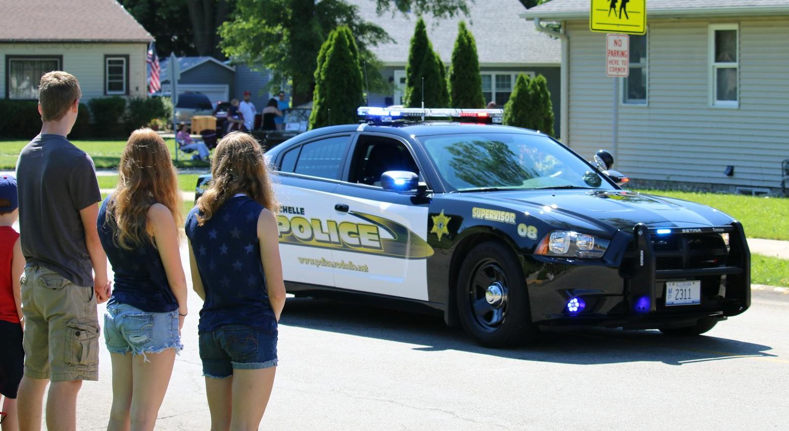 people looking at police car passing through neighbourhood